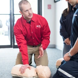 A CPR instructor teaching two students BLS and chest compressions on a manikin.