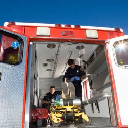 Two EMS providers helping a patient in the back of an ambulance.
